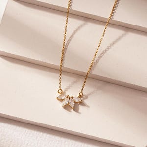 May include: A delicate gold chain necklace with a small pendant featuring a cluster of clear marquise-shaped stones.