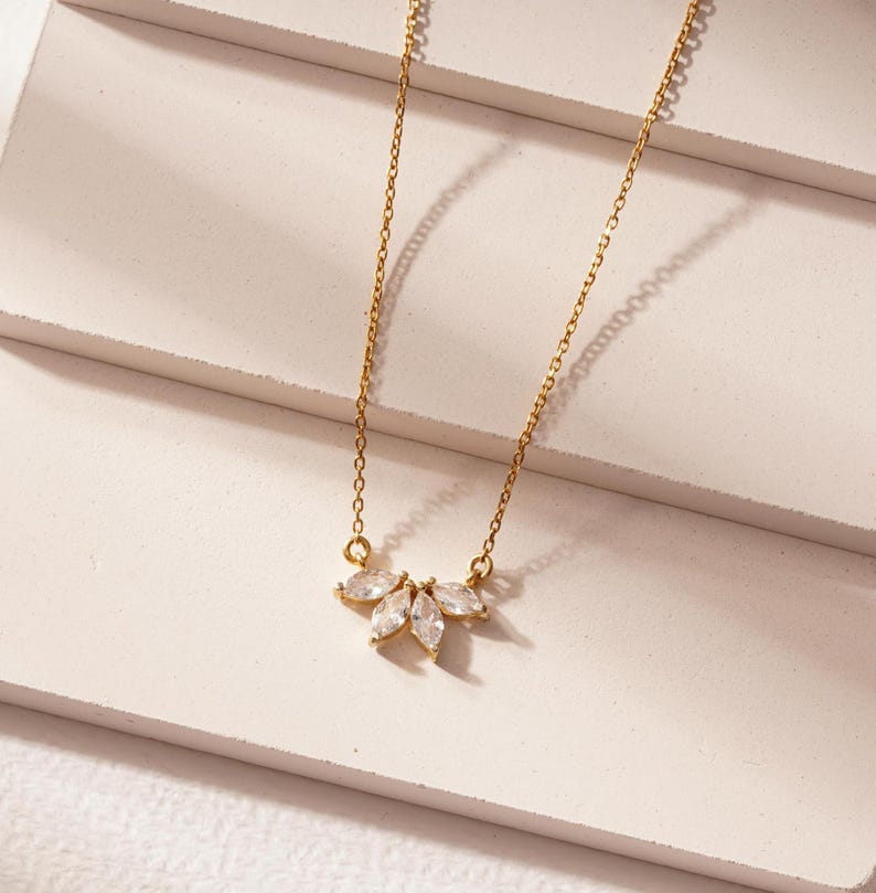 May include: A delicate gold chain necklace with a small pendant featuring a cluster of clear marquise-shaped stones.