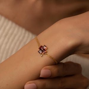 Könnte beinhalten: Ein goldenes Kettenarmband mit einem vierblättrigen Kleeblatt-Anhänger mit roten Edelsteinen.