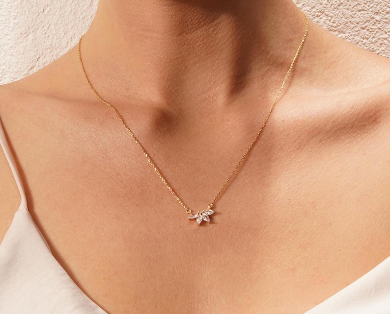 May include: A delicate gold chain necklace with a small, sparkling diamond pendant in the shape of a cluster of leaves.