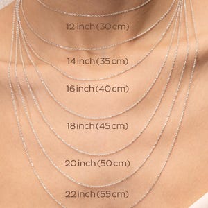 May include: A close-up of a model wearing seven different silver chain necklaces, each with a different length. The lengths are labeled in inches and centimeters, ranging from 12 inches (30 cm) to 24 inches (60 cm).