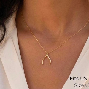 May include: A gold-coloured necklace featuring a wishbone-shaped pendant suspended on a delicate chain. The text in the corner states: Fits US Ring Sizes 3-9. The necklace is worn against a white collared shirt, highlighting the metallic finish.