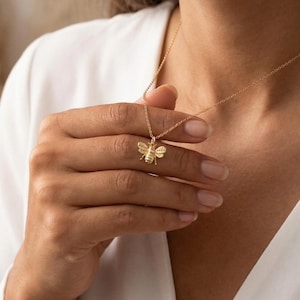 Op de afbeelding: Een gouden bijenhangersketting. De bijenhanger is gedetailleerd met vleugels en lichaamssegmenten. De ketting zit aan een fijne ketting. De achtergrond is een zachte, neutrale kleur.