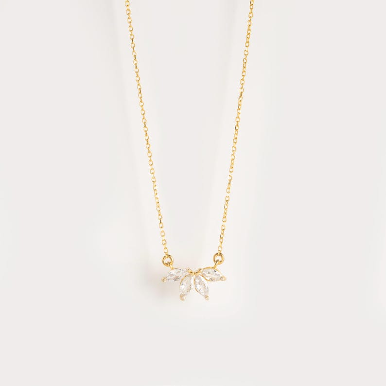 May include: A gold chain necklace with a delicate pendant featuring a cluster of clear marquise-shaped stones.