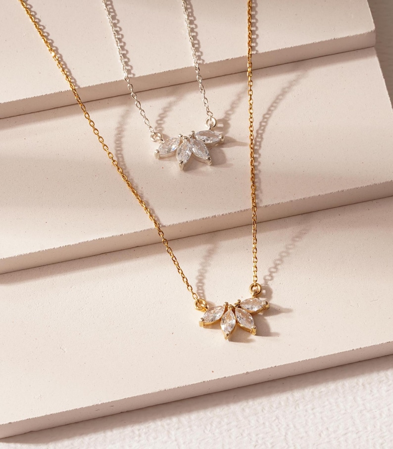 May include: Two delicate necklaces with a cluster of marquise-shaped clear stones in a flower-like design. One necklace is gold and the other is silver.