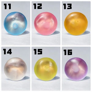 May include: A grid of six translucent, spherical objects labeled 11 through 16. The spheres appear in blue, pink, yellow, white, lime green, and purple. Each smooth, round item casts a distinct shadow, showcasing a glossy, semi-transparent finish.