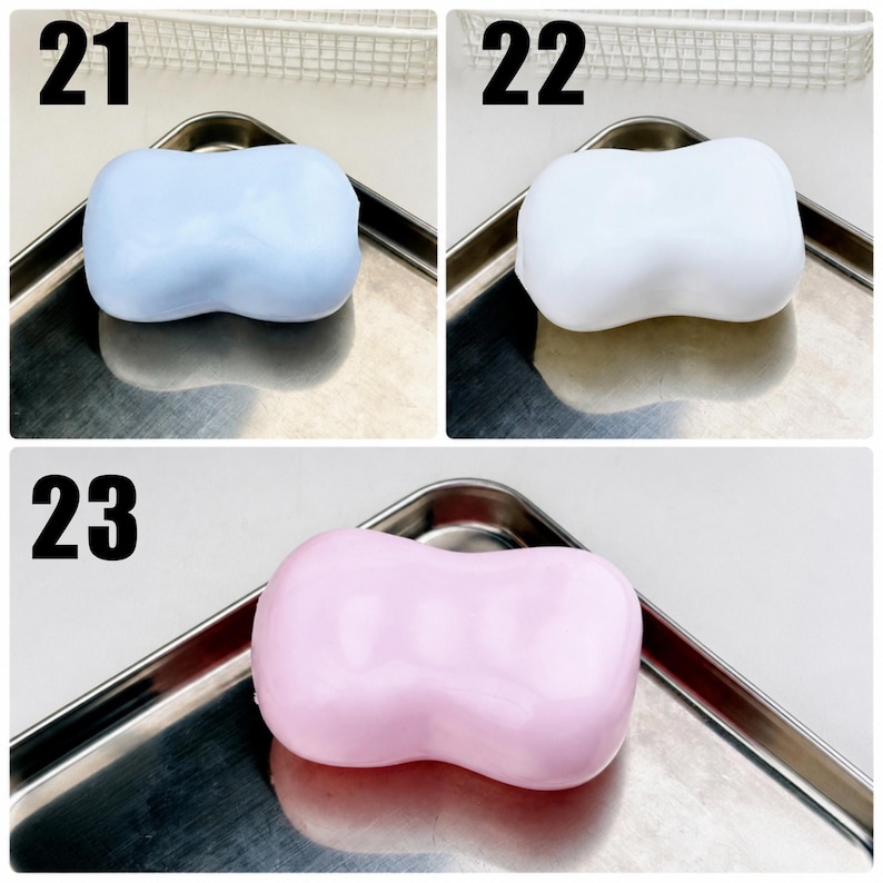May include: Three smooth, rectangular bars of soap with rounded edges and a central indentation. Item 21 is light blue, item 22 is white, and item 23 is light pink. Each bar is displayed individually on a metallic tray with a reflective surface.