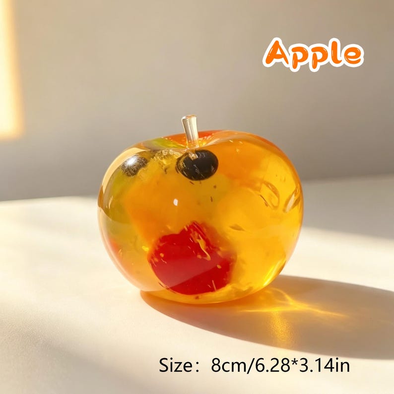 May include: A translucent, amber-colored apple-shaped object with embedded colorful fruit pieces, including a prominent red segment and dark spots. The text 'Apple' appears above, and the text 'Size: 8cm/6.28*3.14in' is printed below the object.