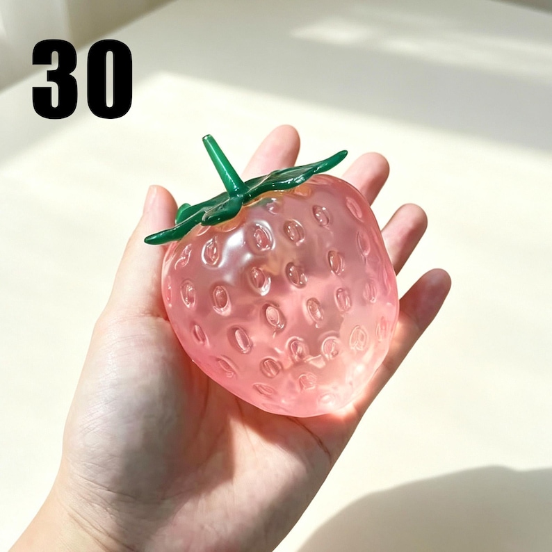 May include: A translucent pink strawberry-shaped object with a green stem and leaves on top. The surface features small indentations mimicking strawberry seeds. The number 30 is printed in black in the upper left corner of the image.