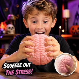 May include: A pink, brain-shaped stress relief toy with a textured, anatomical surface. The toy is held in both hands and is being squeezed. The text "SQUEEZE OUT THE STRESS!" is printed in black and pink on the lower left side of the image.