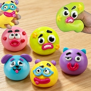 May include: A collection of colorful, expressive stress balls in various shapes and colors. The balls feature cartoonish faces with exaggerated features like large eyes, open mouths, and playful accessories. The collection includes yellow, pink, blue, green, and purple balls.