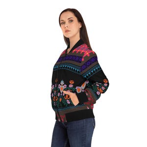 Könnte beinhalten: Eine schwarze Bomberjacke mit einem bunten floralen und geometrischen Muster. Die Jacke hat einen Reißverschluss und zwei Taschen.