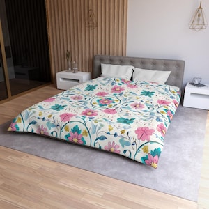 Könnte beinhalten: Eine Bettbezug mit floralem Muster mit rosa, türkisfarbenen und gelben Blumen und grünen Ranken auf cremefarbenem Hintergrund. Die Bettwäsche liegt auf einem grauen Bett mit weißen Kissen in einem Schlafzimmer mit Holzverkleidung.