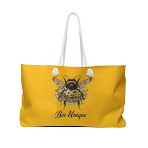 Könnte beinhalten: Eine gelbe Tragetasche mit weißen Seilgriffen zeigt eine Biene mit floralen Akzenten und dem Text "Bee Unique".