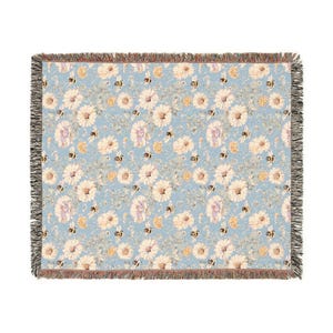 Könnte beinhalten: Eine gewebte Wolldecke mit blauem Hintergrund und einem Muster aus weißen Gänseblümchen und gelben Bienen.