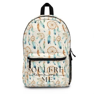 Könnte beinhalten: Weißer Canvas-Rucksack mit einem Muster aus Traumfängern und Federn in Blautönen, Braun und Gold. Der Text "Soulfree time out ME" ist auf der Vorderseite des Rucksacks aufgedruckt.