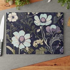 Könnte beinhalten: Rechteckiges Schneidebrett mit floralem Design. Das Brett zeigt weiße, hellblaue und violette Blumen mit grünen Blättern auf einem dunkelblauen Hintergrund. Der Text "SOULFREE time out WE" ist sichtbar.