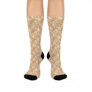 Könnte beinhalten: Ein Paar beigefarbene Socken mit einem weißen Blumenmuster. Die Socken sind aus einem weichen, bequemen Material gefertigt und haben eine schwarze Ferse und Spitze.