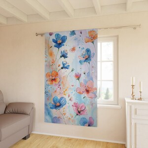 Könnte beinhalten: Ein Vorhang mit Aquarelldruck, der ein Blumenmuster mit blauen, rosa und orangefarbenen Blumen auf hellblauem Hintergrund zeigt.
