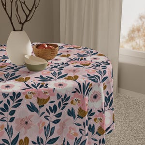 Könnte beinhalten: Eine runde rosa Tischdecke mit einem Blumenmuster mit rosa, weißen und goldenen Blumen, dunkelblauen Blättern und weißen Punkten.