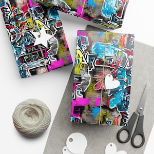 Könnte beinhalten: Buntes Geschenkpapier mit Graffiti-Design. Das Papier zeigt eine Vielzahl von Farben, darunter Pink, Blau, Gelb und Grün. Das Design enthält Buchstaben, Zahlen und Symbole. Das Papier ist mit Schnur gebunden und hat ein weißes herzförmiges Etikett.