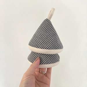May include: A black and white gingham pot holder with a cream-coloured trim and a loop for hanging. The pot holder is in a tree shape. The pot holder is made of fabric.