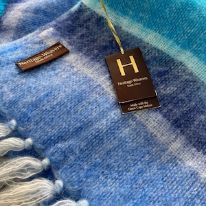 Può includere: Una coperta in mohair blu e bianca con frange. La coperta ha un'etichetta che recita "Heritage-Weavers South Africa". La coperta è realizzata con il miglior mohair del Capo.