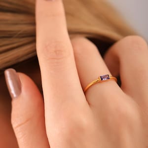 May include: A gold ring with a small, rectangular purple gemstone.