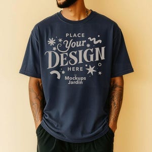 Pode incluir: Camiseta azul marinho com o texto "PLACE YOUR DESIGN HERE Mockups Jardin" em branco. A camiseta é um design de maquete, ideal para mostrar obras de arte ou logotipos personalizados. O modelo está vestindo calças pretas.