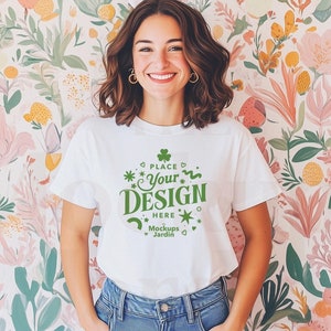 Könnte beinhalten: Ein weißes T-Shirt mit einem grünen Kleeblatt und dem Text "Place Your Design Here" und "Mockups Jardin". Das Shirt wird von einer Person mit braunen Haaren und einem weißen Hasenohren-Stirnband getragen. Die Person steht vor einer floralen Tapete.
