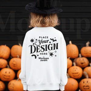 May include: A white sweatshirt with the text "PLACE Your DESIGN HERE Mockups Jardin" on the back. A black witch hat is worn on the head. The background features a wall of orange pumpkins.
