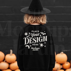 May include: A child wearing a black witch hat and a black sweatshirt with the text "PLACE YOUR DESIGN HERE" in white. The background features a black wall and several orange pumpkins, creating a Halloween theme.