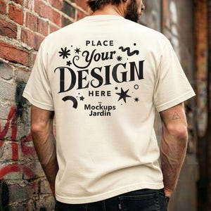 Könnte beinhalten: Cremefarbenes T-Shirt mit dem schwarzen Text "PLACE Your DESIGN HERE" sowie Stern- und Wirbelgrafiken. Das Mockups Jardin-Logo befindet sich unten. Das Shirt hat kurze Ärmel.