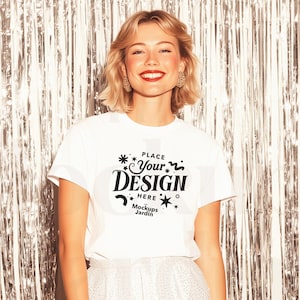 May include: A white t-shirt with the text "PLACE Your DESIGN HERE Mockups Jardin" in black. The model is wearing white pants and is standing in front of a silver, shiny backdrop.