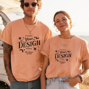 May include: Two people wearing peach-colored t-shirts with rolled-up sleeves. The shirts feature a black graphic that says "PLACE YOUR DESIGN HERE" with the text "Mockups Jardin" below. They are standing in front of a vintage camper.