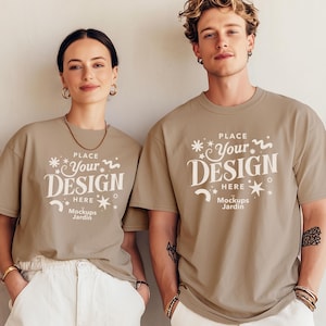 Op de afbeelding: Twee mensen dragen taupekleurige t-shirts met de witte tekst "PLACE Your DESIGN HERE Mockups Jardin". De shirts worden gecombineerd met een witte broek. De achtergrond is een neutrale, lichtgekleurde muur.