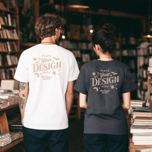 Pode incluir: Duas pessoas vestindo camisetas brancas e cinza carvão com o texto "PLACE YOUR DESIGN HERE" em uma fonte decorativa. As camisas são de manga curta e as pessoas estão em uma livraria.