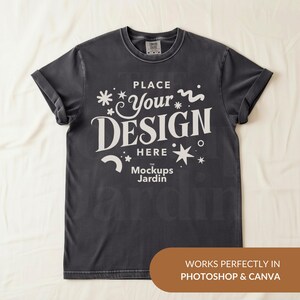 May include: A charcoal gray short-sleeve t-shirt featuring the white text PLACE YOUR DESIGN HERE and the text The Mockups Jardin. The shirt has a crew neckline and a tag at the inner collar. A brown rectangular graphic is at the bottom right.