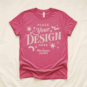 Op de afbeelding: Een magenta t-shirt met opgerolde mouwen. Het shirt toont de tekst "PLACE Your DESIGN HERE" in lichtbeige, samen met decoratieve sterren en krullen. De tekst "The Mockups Jardin" is ook aanwezig.