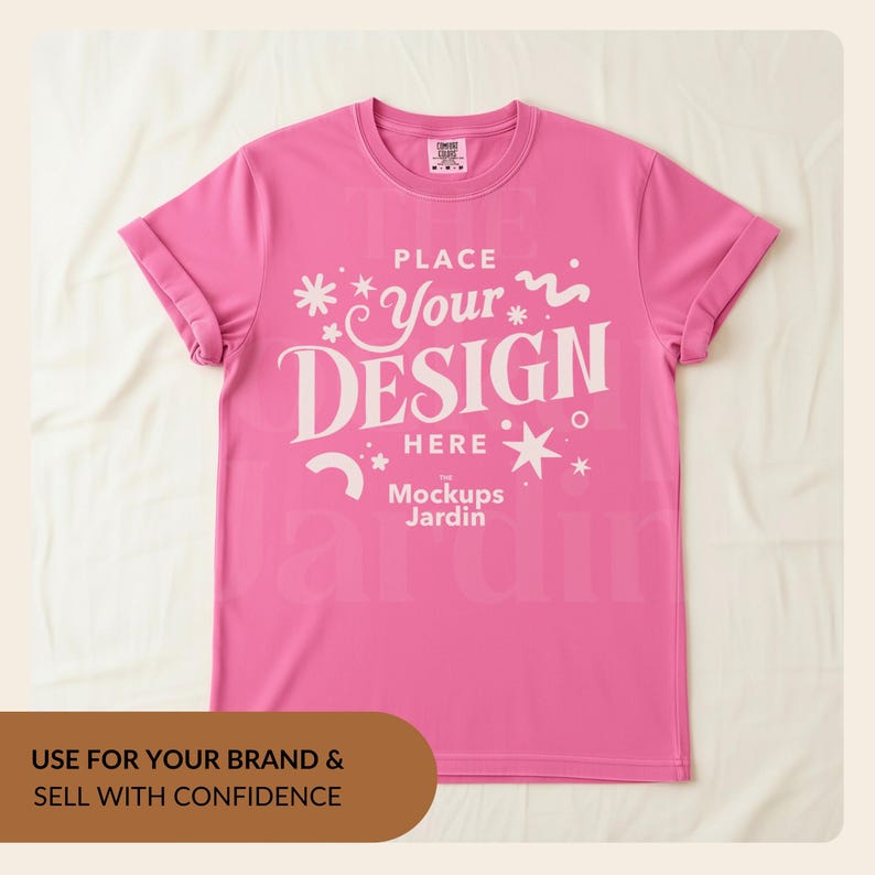 May include: A bright pink short-sleeved t-shirt featuring white graphic text that reads THE PLACE YOUR DESIGN HERE and Mockups Jardin, surrounded by various small white star and squiggle icons, with a crew neckline and rolled sleeves.