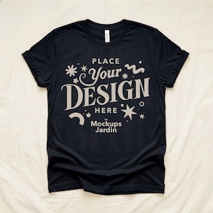 May include: A black t-shirt with rolled-up sleeves. The shirt features the text "PLACE Your DESIGN HERE" in a stylized font, along with decorative star and swirl elements. The words "The Mockups Jardin" are at the bottom of the design.