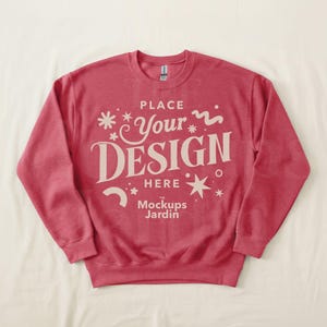 May include: A red sweatshirt with the text "PLACE YOUR DESIGN HERE" in a decorative font. The sweatshirt has a crew neck and long sleeves. The Mockups Jardin logo is at the bottom.