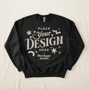 May include: Black crewneck sweatshirt with the text "PLACE Your DESIGN HERE" in a decorative font. The Mockups Jardin logo is below the text. The sweatshirt is displayed on a white surface.