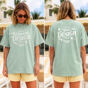 Könnte beinhalten: Ein kurzärmeliges T-Shirt in Salbeigrün mit weißem Text auf der Vorder- und Rückseite, der "PLACE YOUR DESIGN HERE" sowie "Mockups Jardin" und verschiedene kleine Stern- und Schnörkelgrafiken zeigt. Das Shirt hat einen Rundhalsausschnitt.