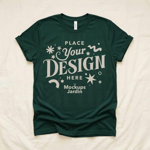 May include: Dark green t-shirt with rolled sleeves. The shirt features the text "PLACE Your DESIGN HERE" in a stylized font, along with decorative star and floral elements. The brand name "The Mockups Jardin" is also visible.