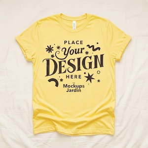 May include: A yellow t-shirt with rolled-up sleeves. The shirt features the text "PLACE Your DESIGN HERE" in a decorative font, along with star and swirl graphics. The Mockups Jardin logo is at the bottom.