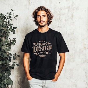 Op de afbeelding: Een zwart T-shirt met korte mouwen en een bruin grafisch ontwerp met de tekst "Place Your Design Here" met een ster- en wervelpatroon. De tekst "Mockups Jardin" is ook in het ontwerp opgenomen.
