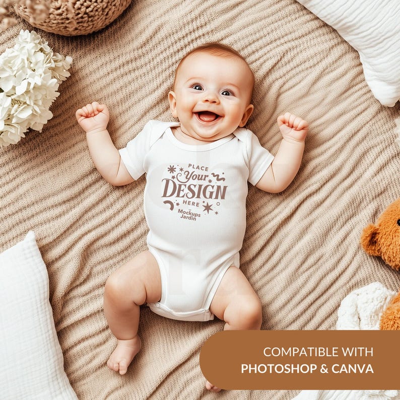 May include: White baby onesie with short sleeves and a brown text overlay that says "Place Your Design Here Mockups Jardin". The onesie is on a brown blanket with a white pillow and a white flower bouquet.