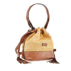 May include: A straw bucket bag with a brown leather bottom and a brown leather top handle. The bag has a drawstring closure and a tassel detail.