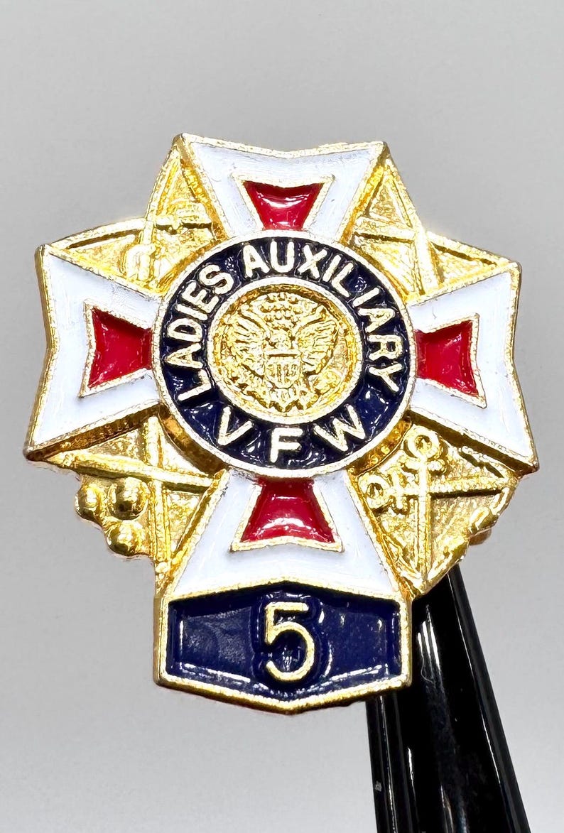 Puede incluir: Un pin dorado con un dise&ntilde;o de cruz, con detalles de esmalte blanco, rojo y azul. El c&iacute;rculo central dice "Ladies Auxiliary VFW" alrededor de un emblema dorado. Una pancarta azul en la parte inferior muestra el n&uacute;mero "5".